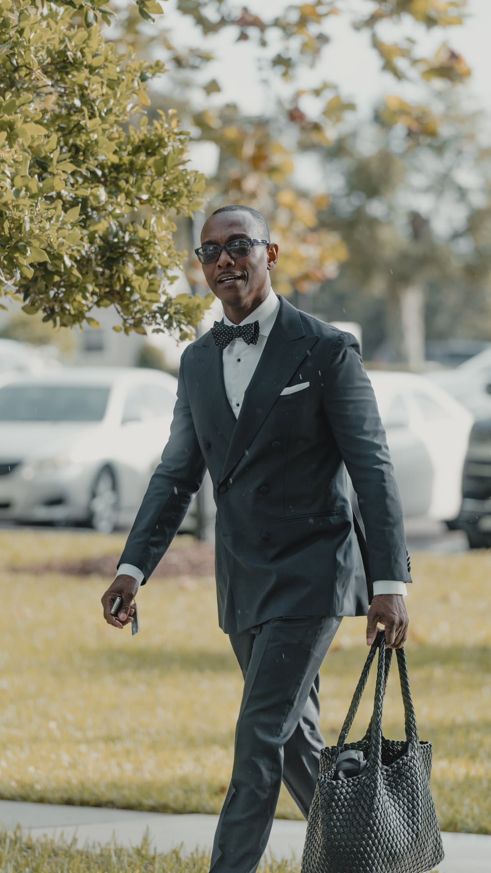 Man in a black suit carrying a woven handbag